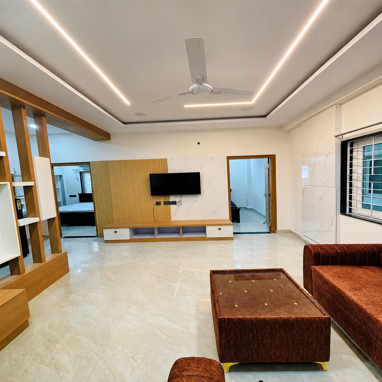 Modern living room, contemporary living room, stylish living room, spacious living space, luxury living room, bright home interior, elegant interior design, modern apartment interior, residential interior, open plan living room, comfortable sofa, brown sofa, modern sofa set, upholstered seating, center table, wooden TV unit, wall mounted TV, entertainment unit, TV wall design, decorative wall panel, wooden wall panel, marble wall finish, glossy flooring, marble flooring, large windows, natural light, modern false ceiling, LED strip lighting, ambient lighting, ceiling fan, modern ceiling design, clean interior, organized living space, minimalist home decor, functional living room, cozy living area, urban home interior, rental home interior, student-friendly accommodation, student living space, student rental home, study-friendly home, working professional accommodation, professional living space, work-life balance home, comfortable rental property, family living room, modern home design, premium home interior, real estate interior.